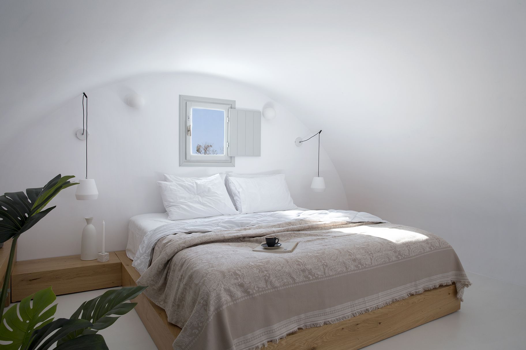 A minimalist bedroom with a bed, bedside lamps, a window, and a plant.