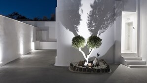 Un edificio moderno de diseño minimalista, con una jardinera de piedra circular que contiene dos árboles y una pequeña escultura.