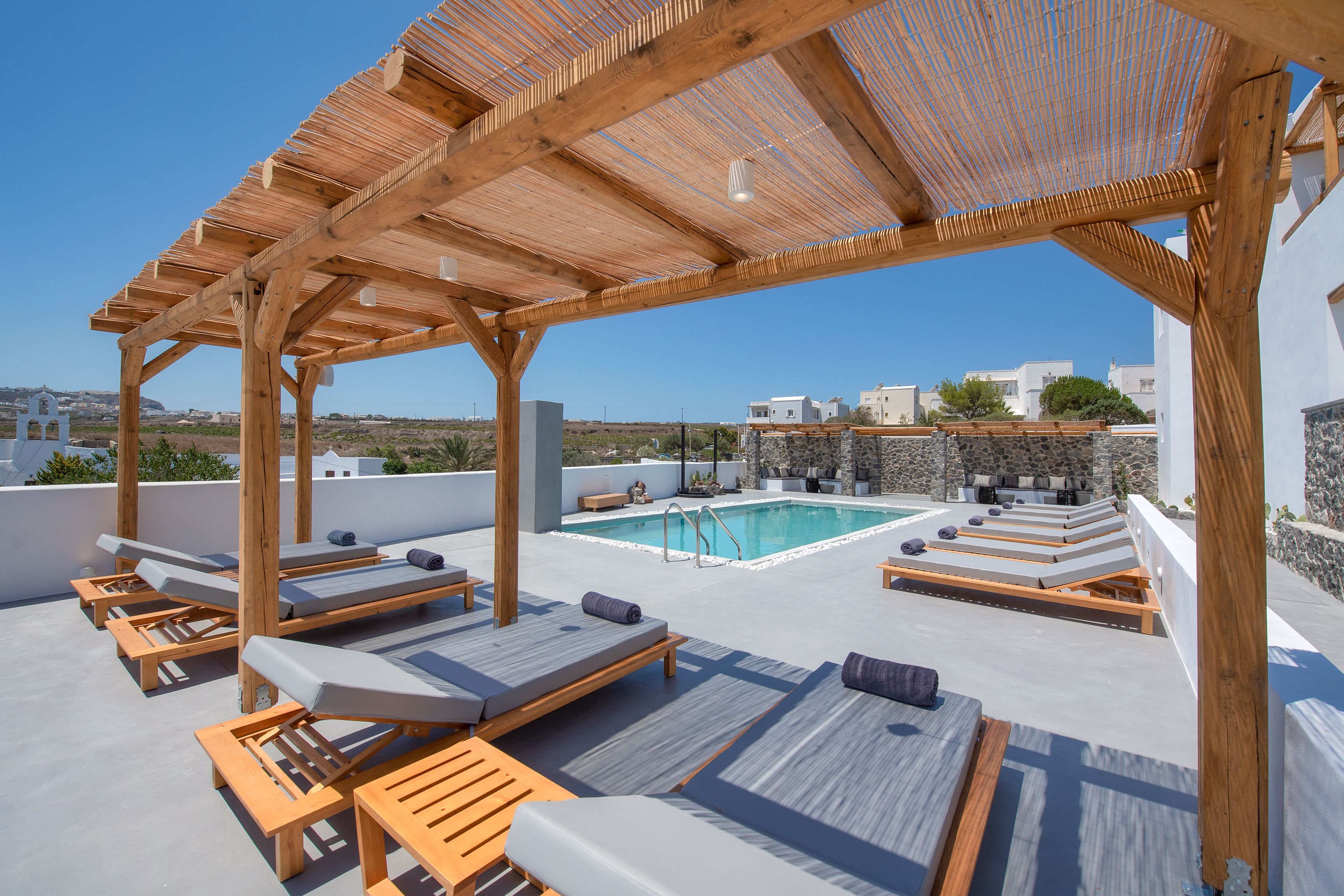 A rooftop terrace with wooden loungers, a pool, and a pergola.