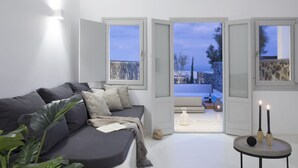 Una sala de estar moderna con un sofá gris, una pequeña mesa redonda con velas y vistas a un paisaje nevado a través de puertas francesas abiertas.