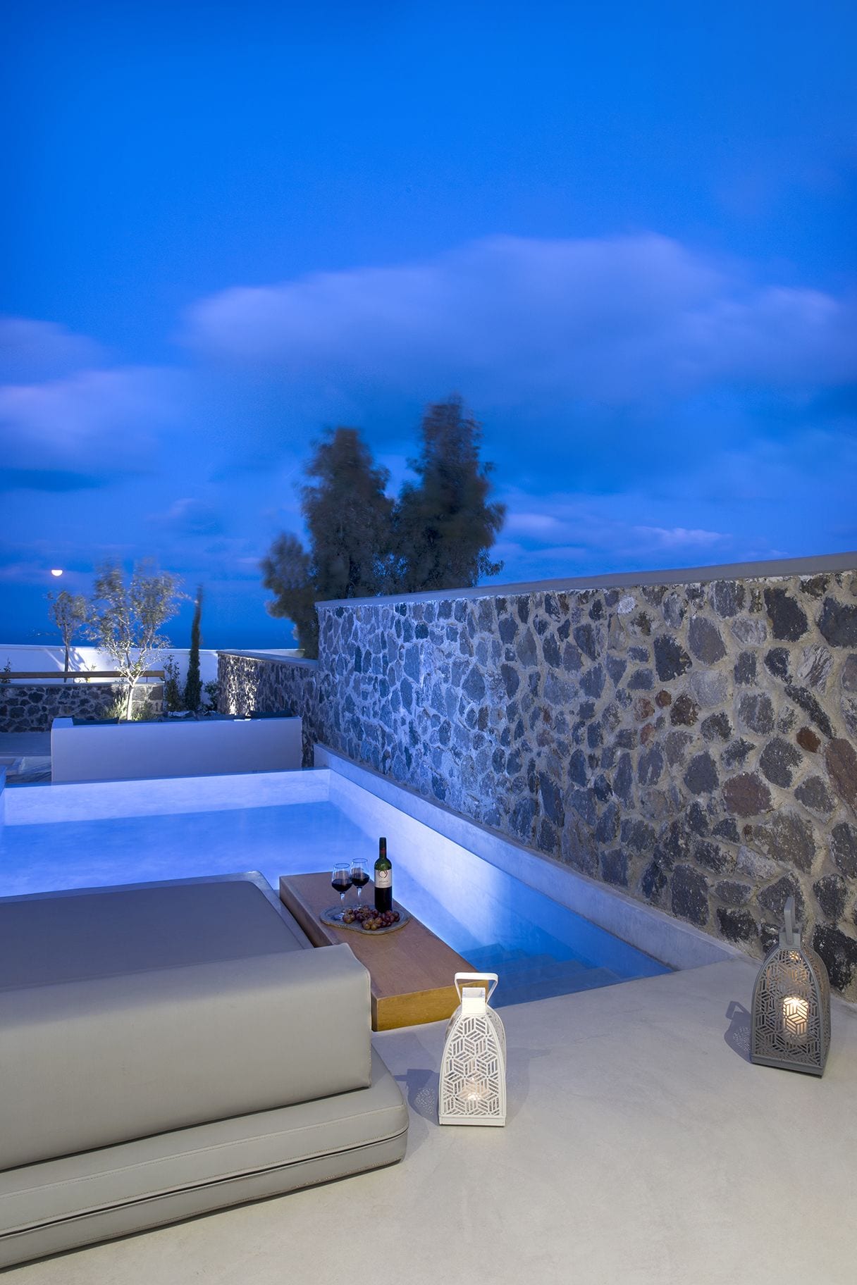 An outdoor seating area with a stone wall, a pool, and a table with drinks and a bottle.