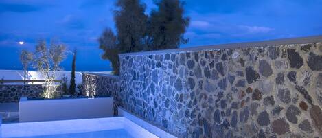 An outdoor seating area with a stone wall, a pool, and a table with drinks and a bottle.