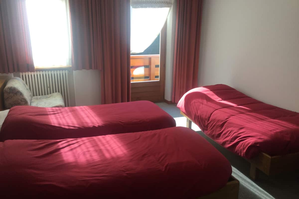 A room with two beds, a wooden bench, a radiator, and a window with curtains.