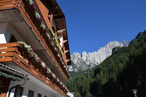 A hotel with wooden balconies adorned with flowers, set against a backdrop of a mountain range. - Hotel Alpenrose (Alleghe)