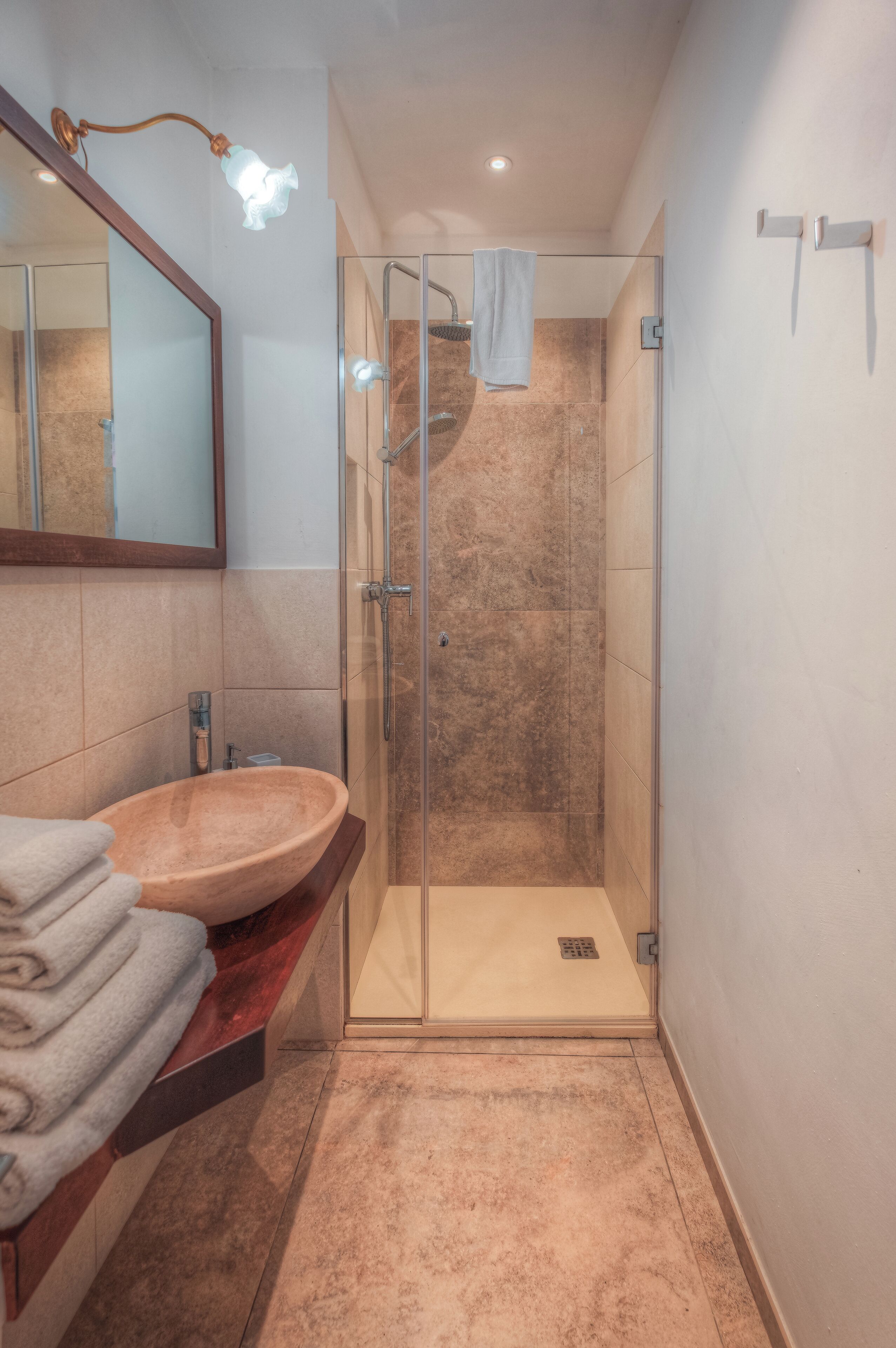 Un bagno con doccia vetrata, mobile lavabo in legno e specchio sopra il lavandino.