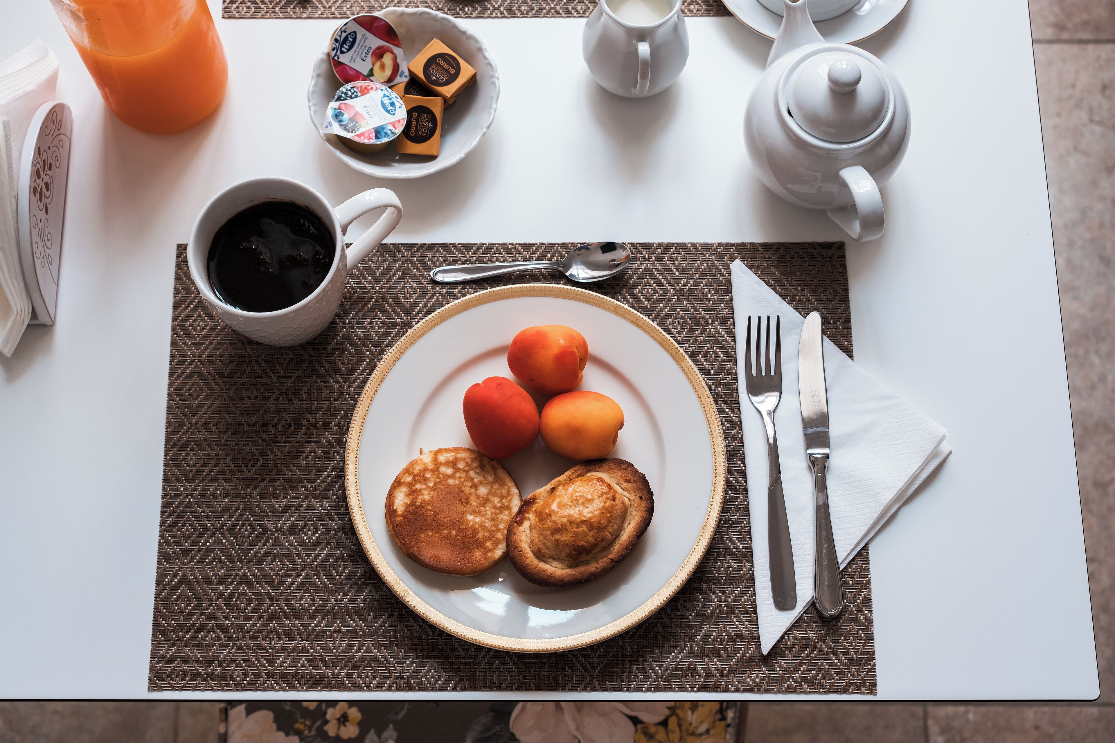 Une table de petit-déjeuner avec une assiette de crêpes, une tasse de café et un bol de fruits.