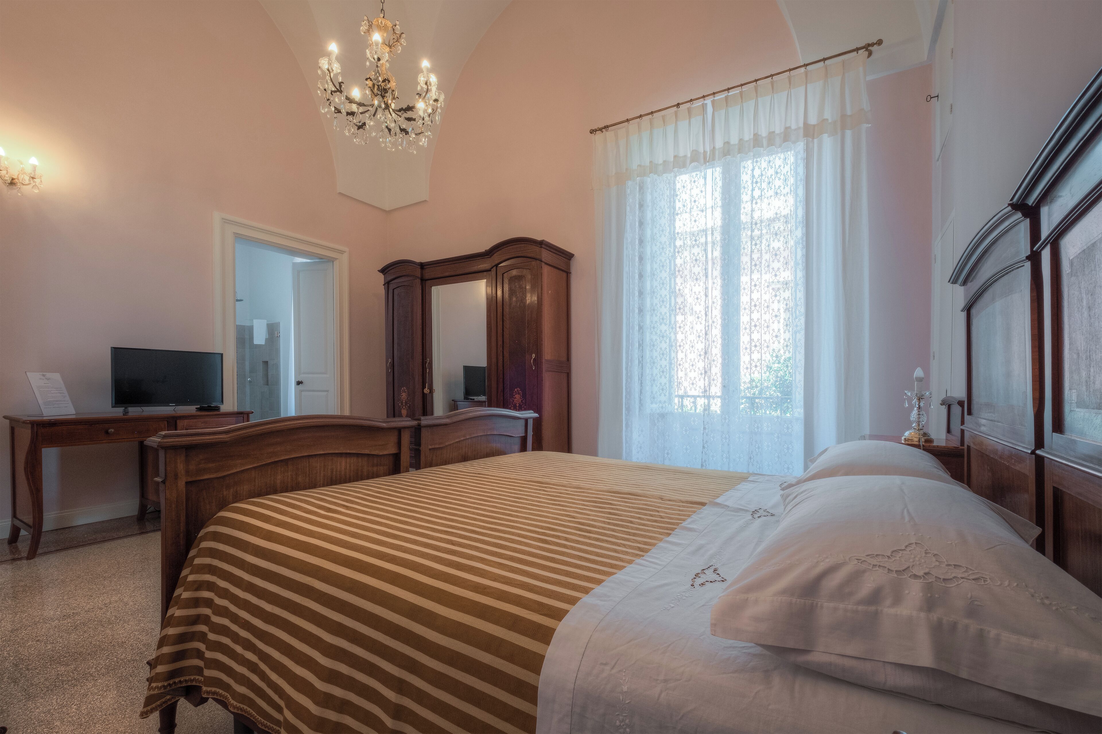 Ein Schlafzimmer mit einem großen Bett, einer Holzkommode, einem Schreibtisch mit Fernseher und einer Kristallleuchtre.
