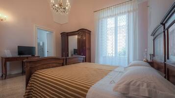 Ein Schlafzimmer mit einem großen Bett, einer Holzkommode, einem Schreibtisch mit Fernseher und einer Kristallleuchtre.