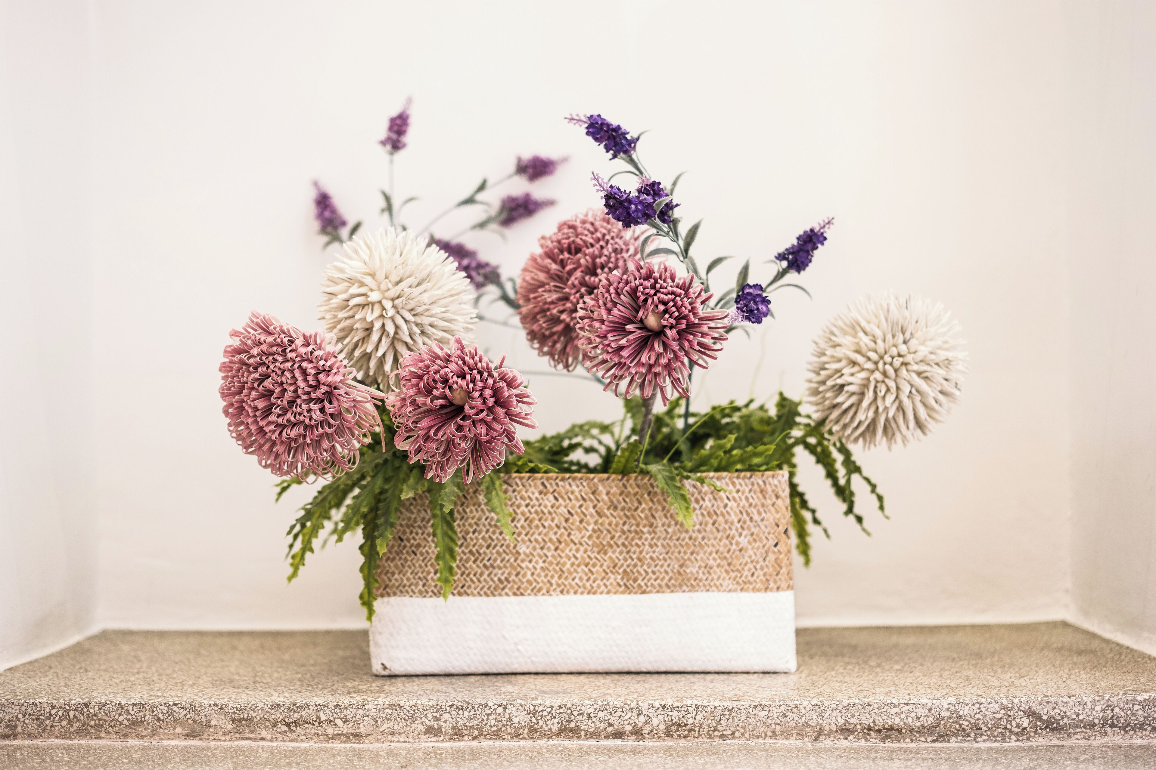 A woven basket containing various flowers on a stone ledge.