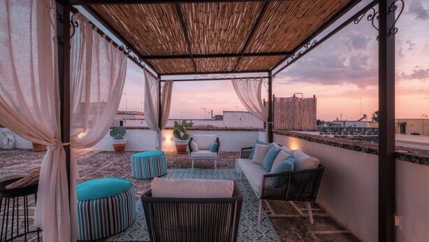 A rooftop terrace with a wooden pergola, cushioned seating, and a potted plant. - Palazzo Vaglio Relais (Nardò)