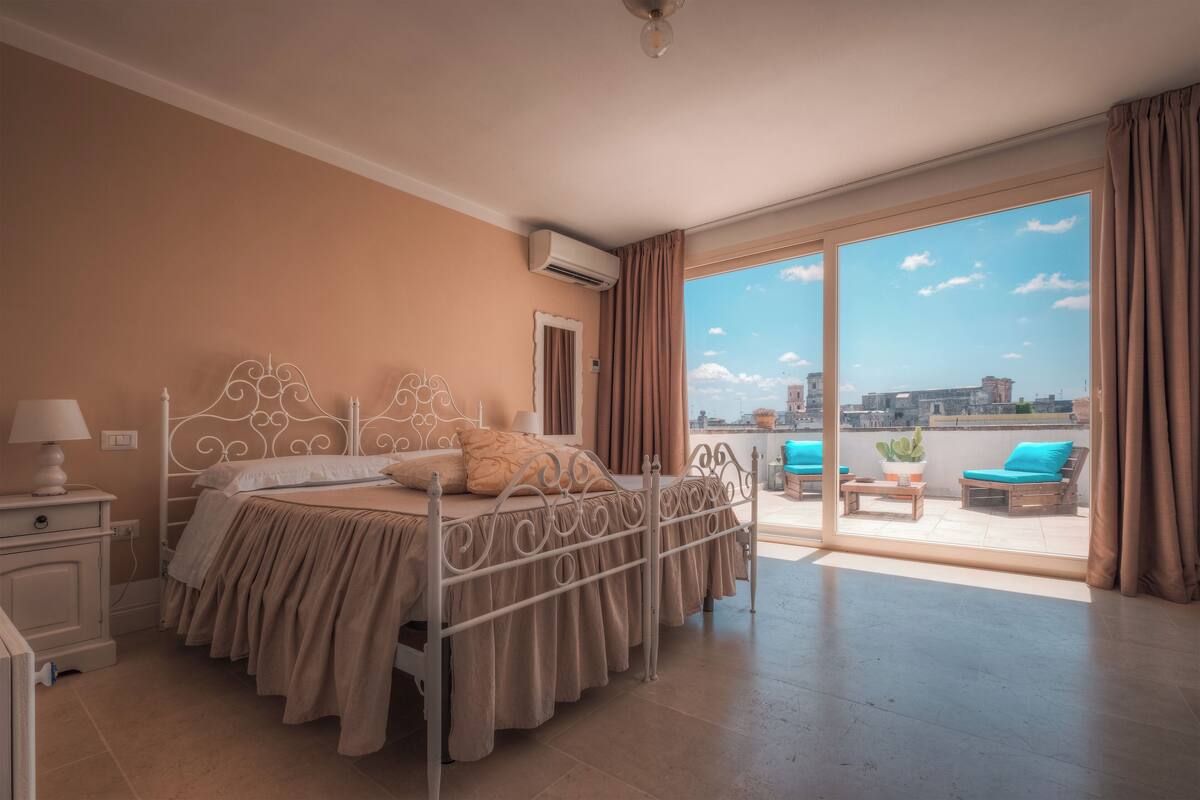 Une chambre avec un lit, une table de chevet, une fenêtre et une vue sur le balcon extérieur.