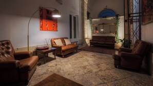 A cozy living room with leather sofas, a coffee table, and a floor lamp. There is a large window with a view of the city. - Palazzo Vaglio Relais (Nardò)
