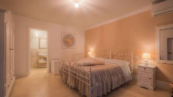 Quarto com cama, mesas de cabeceira, um espelho fixado na parede e porta para um banheiro.