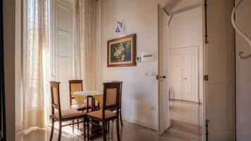 Uma sala de jantar com mesa e cadeiras, um quadro na parede e uma porta que dá para outro cômodo.