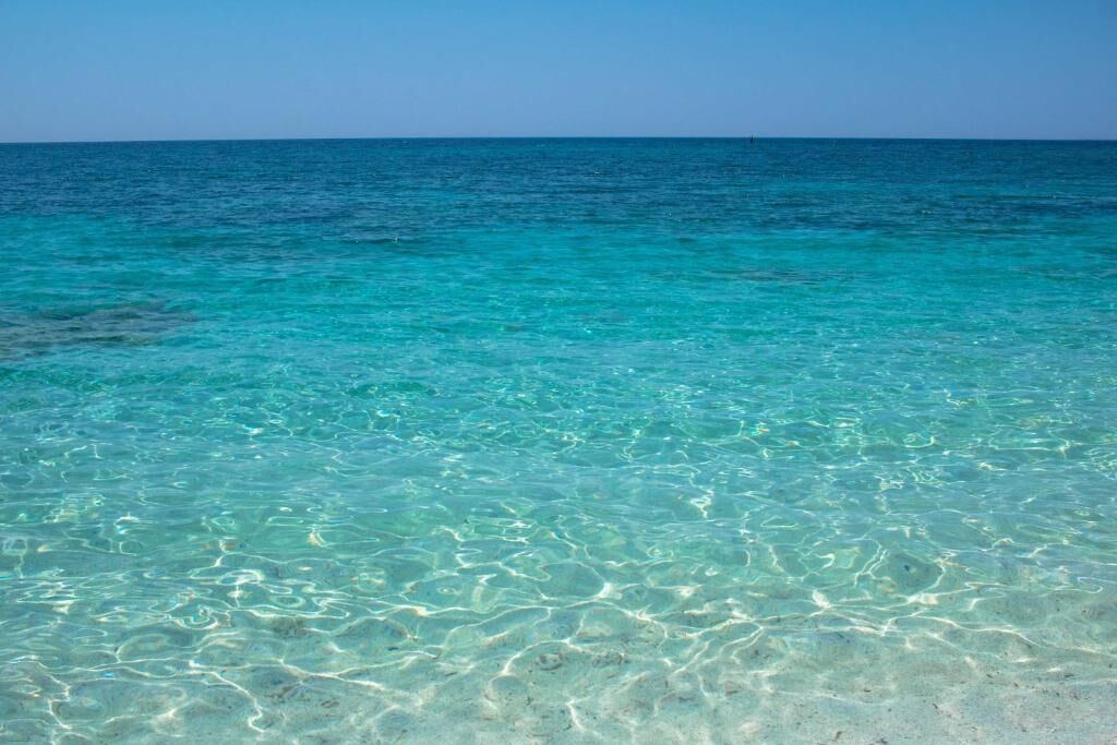 A clear view of a turquoise sea with visible sand patterns on the beach.