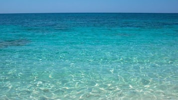 A clear view of a turquoise sea with visible sand patterns on the beach.