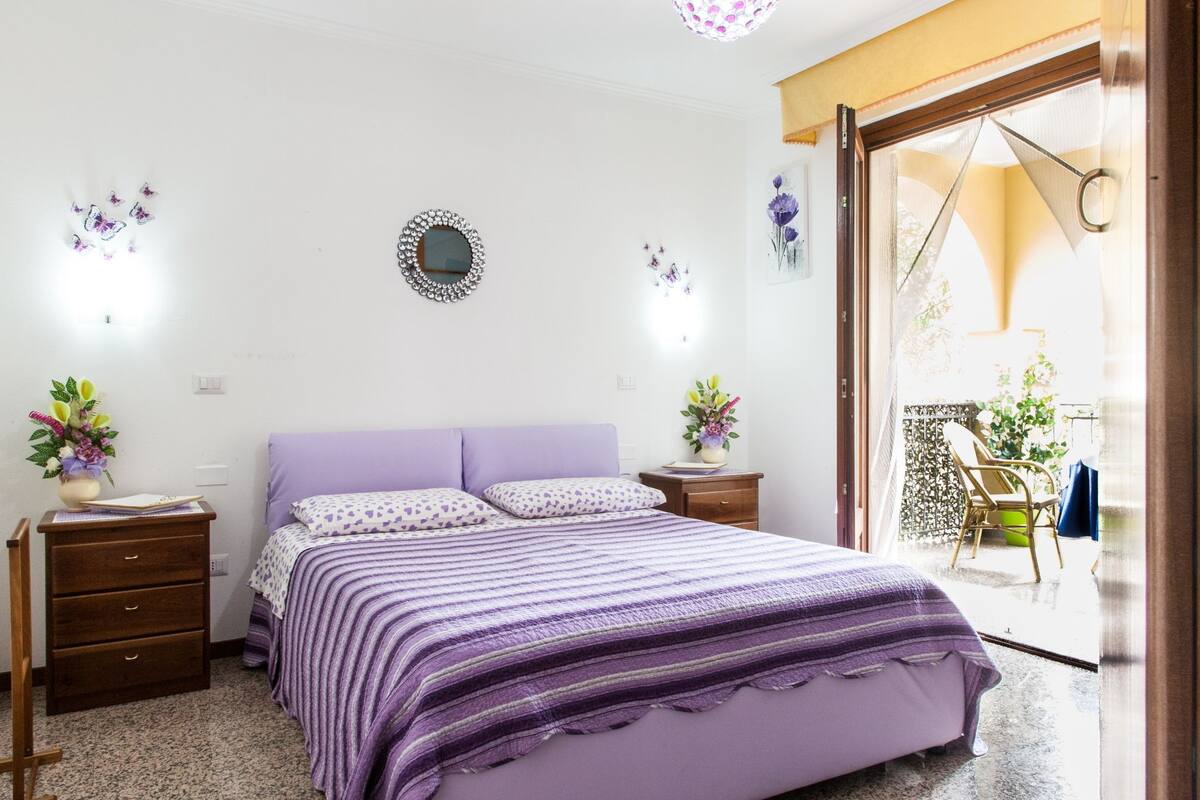 A bedroom with a bed, two nightstands, a dresser, and a window with a view of the outside.