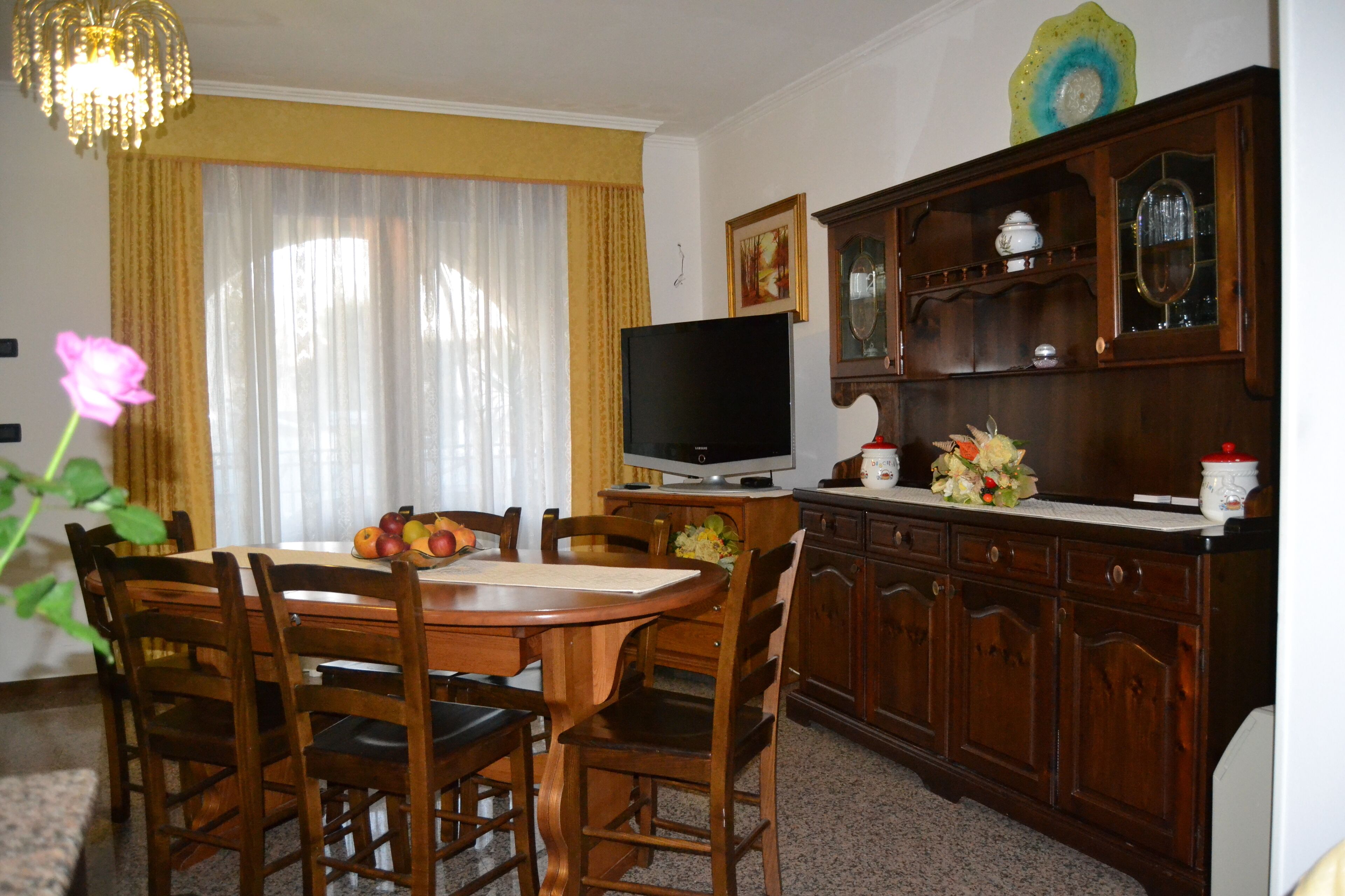 Un comedor con una mesa de madera, sillas, un televisor y un mueble con puertas de vidrio.