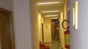 A hallway with a patterned carpet, a fire extinguisher, and a door on the left. - Hotel Centrale (Argenta)