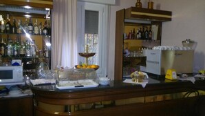 A bar area with shelves of liquor bottles, a refrigerator, and a glass display case with food items. - Hotel Centrale (Argenta)