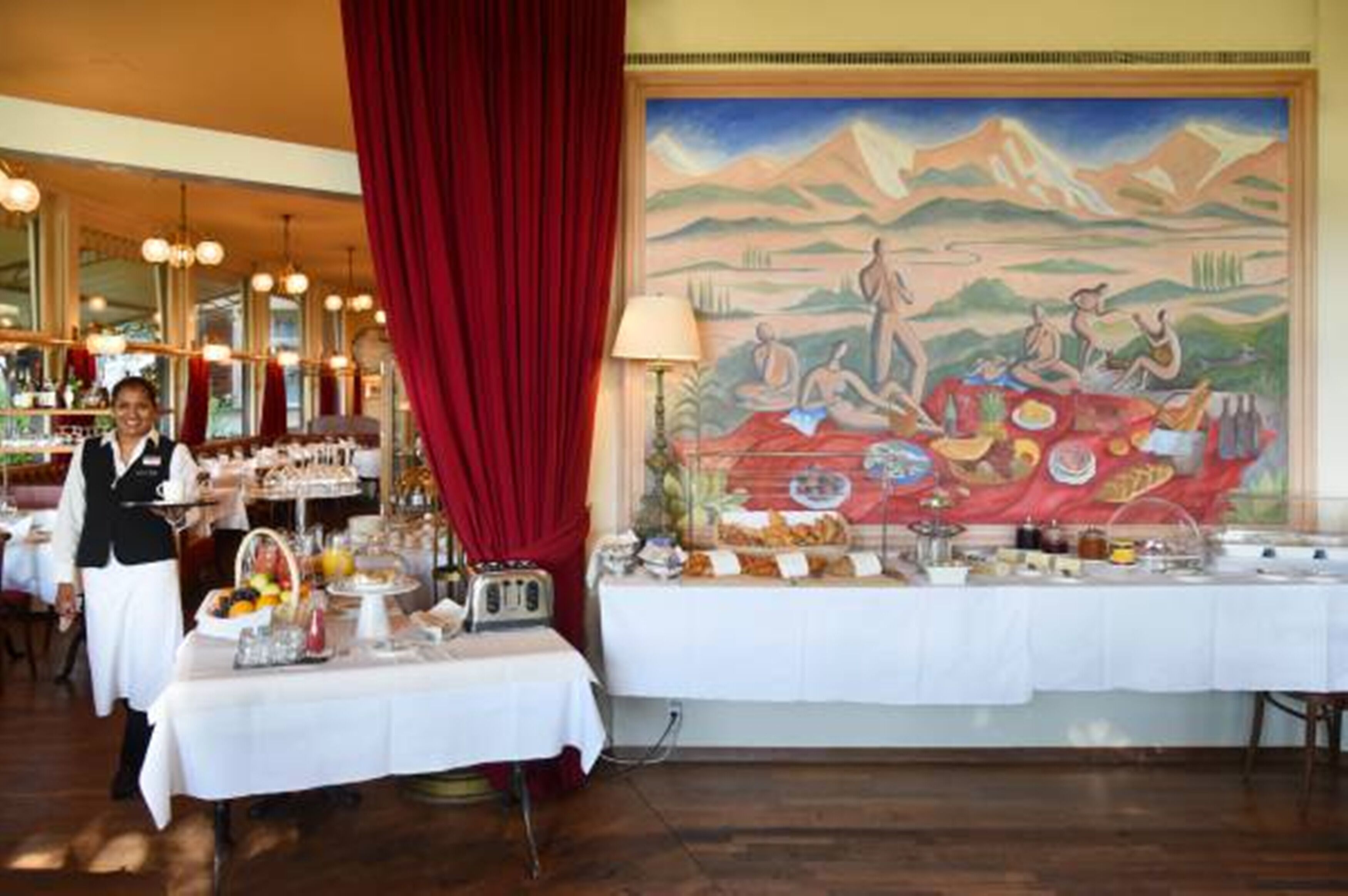A restaurant with a buffet setup, a mural on the wall, and a red curtain.