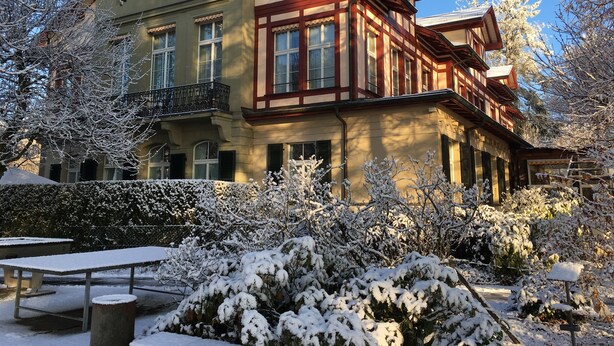 Un edificio de dos pisos con un balcón y un jardín cubierto de nieve.