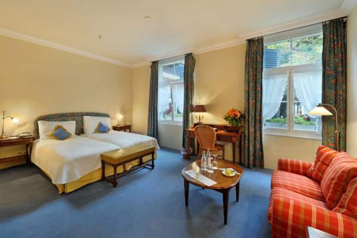 A hotel room with two beds, a desk, a coffee table, and a sofa.