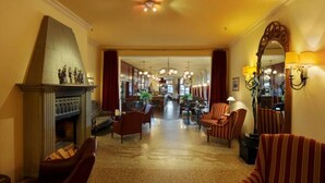 Un hall de hotel con chimenea, sillones a rayas, un candelabro y un espejo.