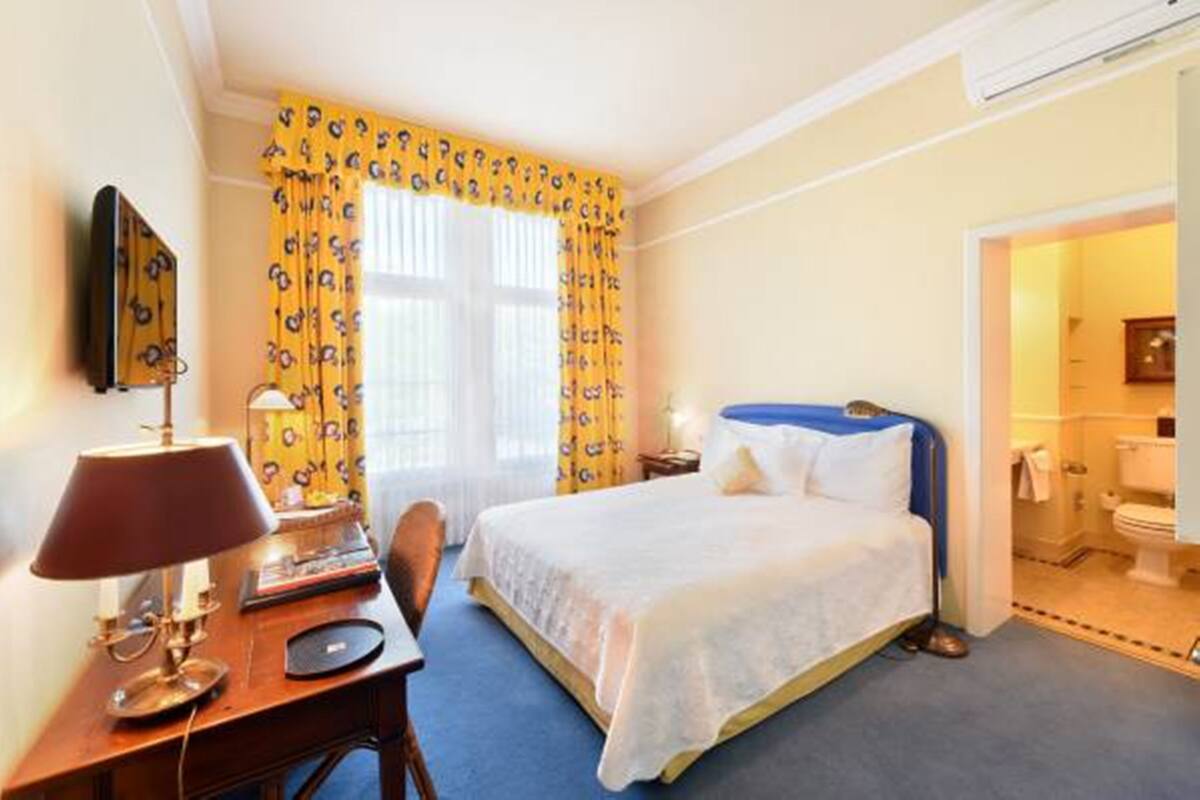 A hotel room with a bed, a desk with a lamp, a chair, and a window with curtains.