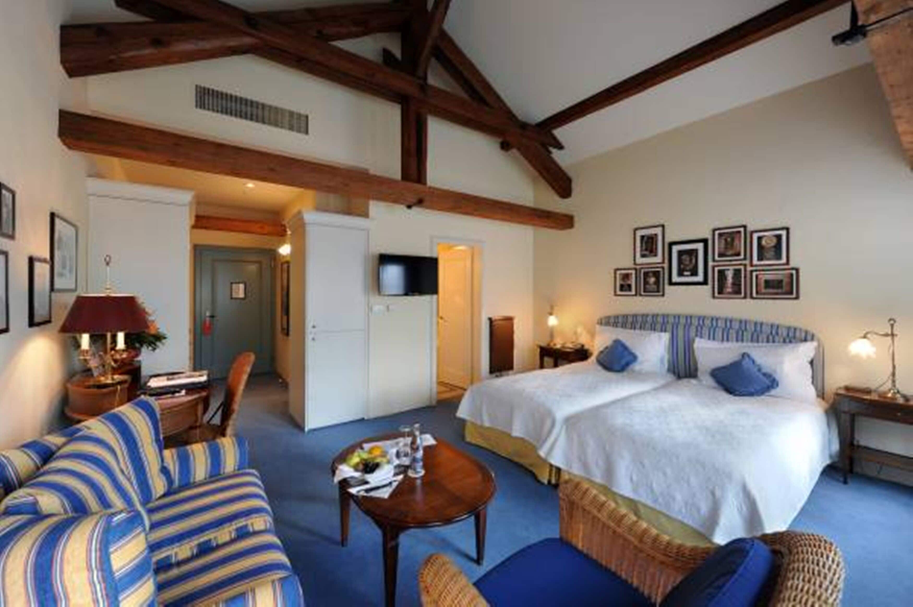 Une chambre d’hôtel avec un grand lit, deux tables de chevet, une télévision et un coin salon comprenant un canapé et un fauteuil.