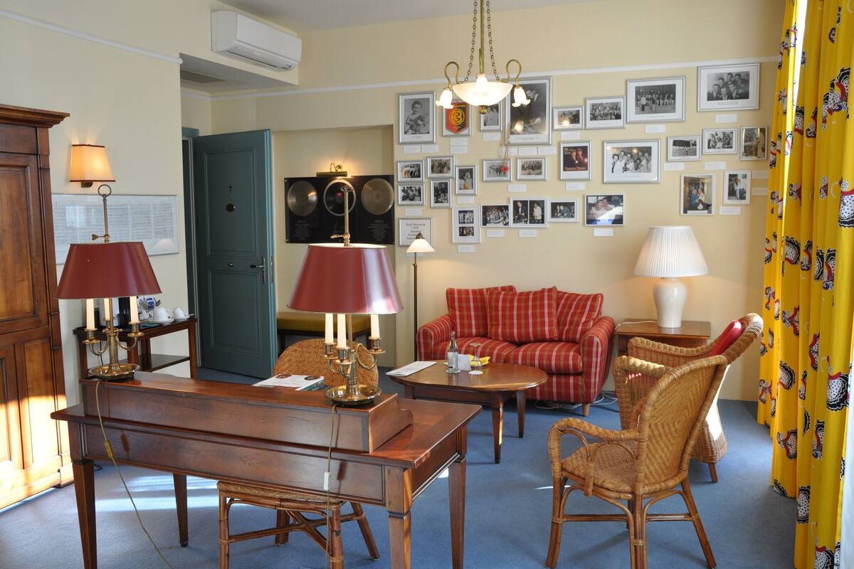 A cozy living room with a wooden table, red lamps, a red sofa, and a wall adorned with framed photos.