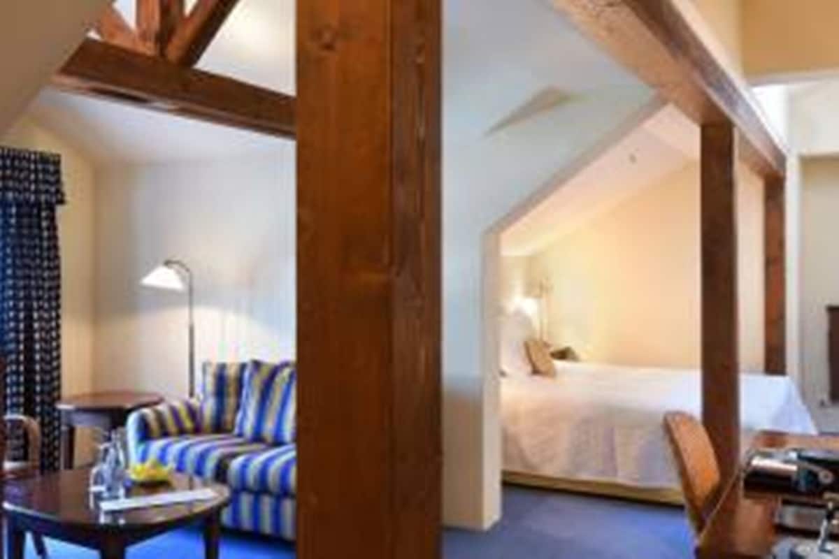 A hotel room with a bed, a sofa, a desk, and a lamp.