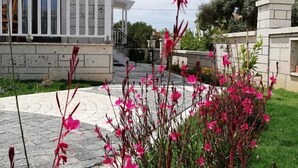 A modern building with a balcony and a garden with pink flowers.