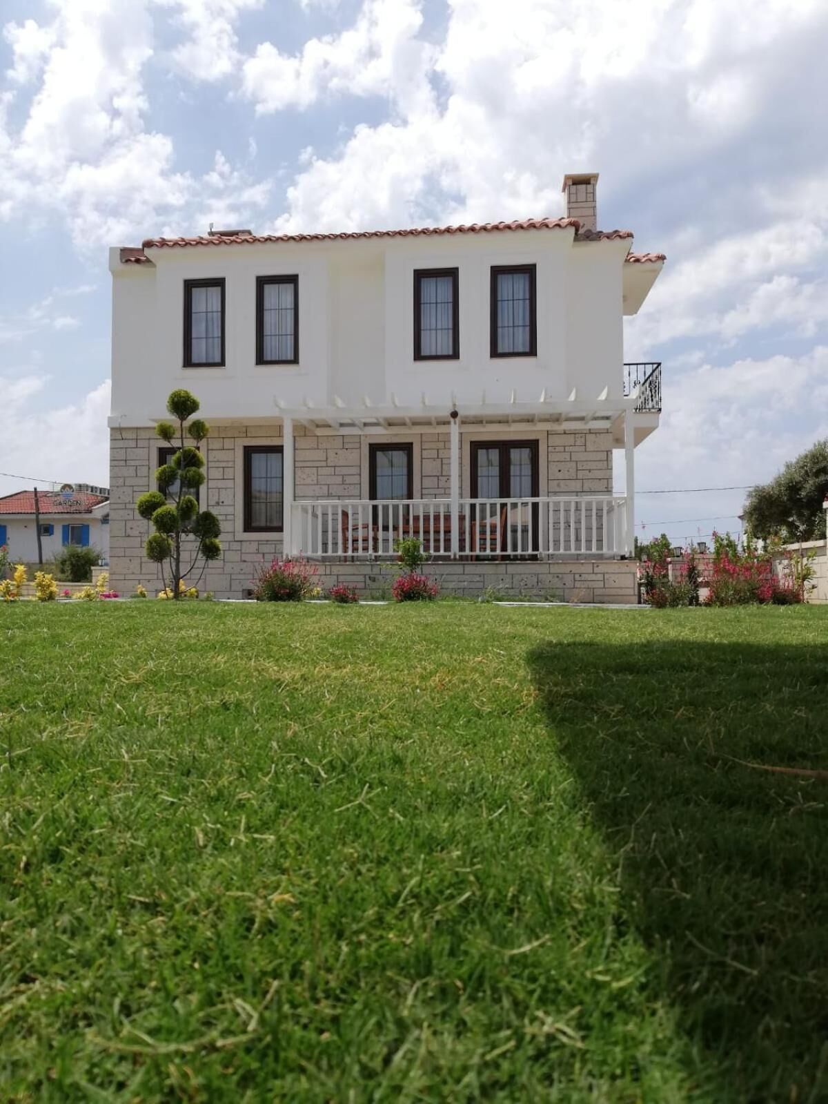 A two-story house with a white facade, a tiled roof, and a small balcony.