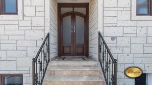 A building entrance with a wooden door, stone steps, and a metal railing.