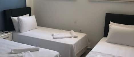 A hotel room with two single beds, a nightstand, a lamp, and a window with blinds.