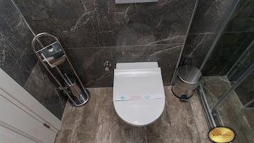 Moderni kylpyhuone, jossa on valkoinen wc-istuin, bidee ja roskakori.