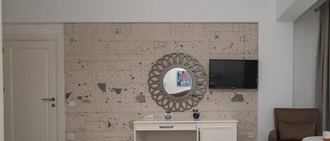 Un dormitorio moderno con un aparador blanco, un espejo redondo, un televisor de pantalla plana en la pared y un sillón marrón.