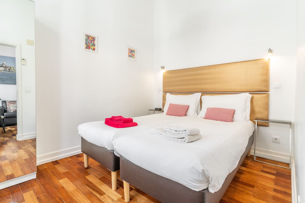 A double bed with white and pink bedding, a wooden headboard, and a small bedside table with a lamp.
