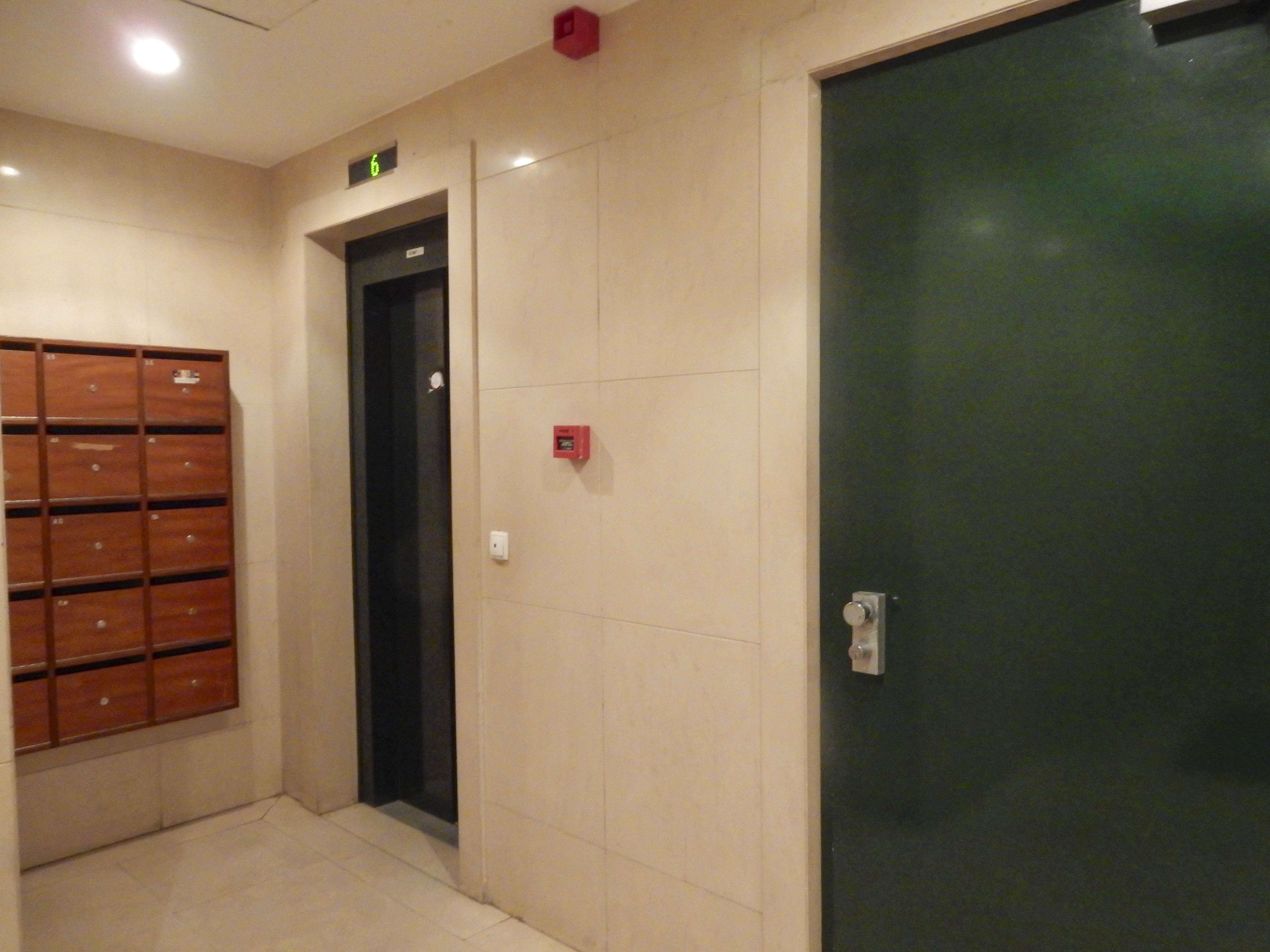 Un pasillo con un mueble de almacenamiento de madera, una puerta con detector de incendios y una puerta oscura.