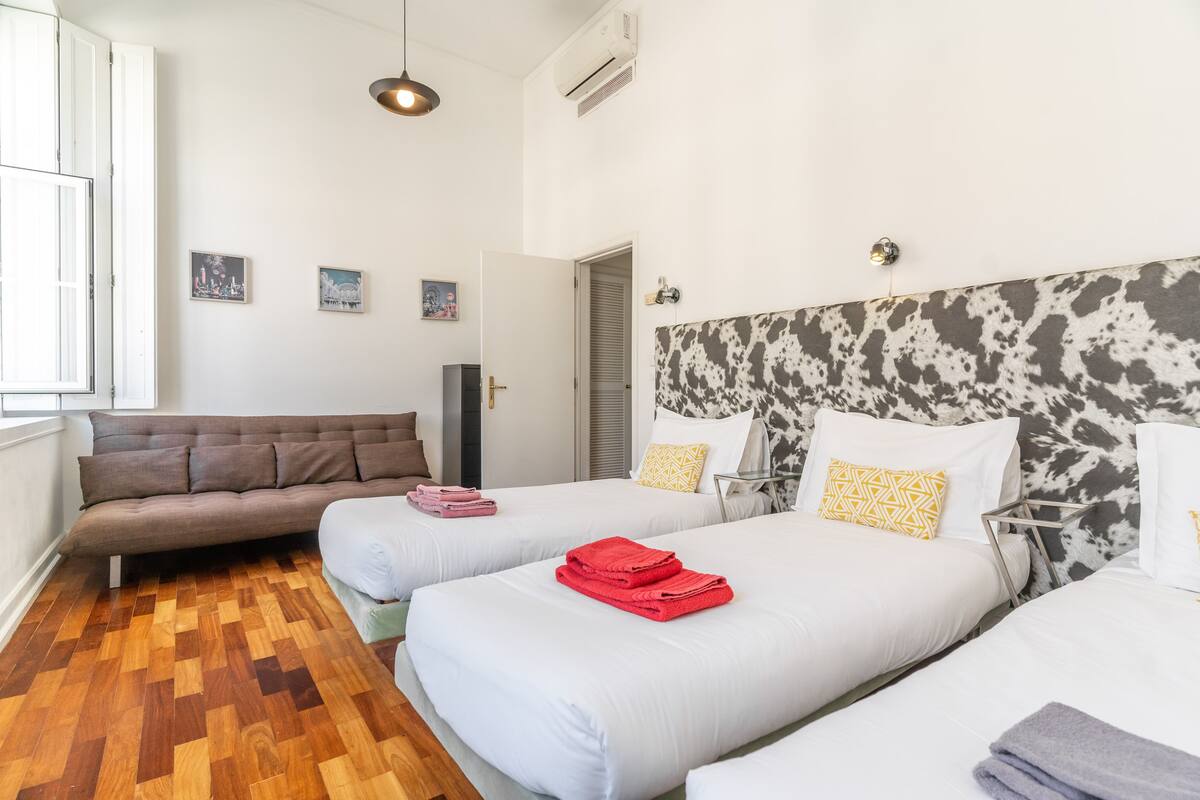 A hotel room with two beds, a sofa, and a wooden parquet floor.