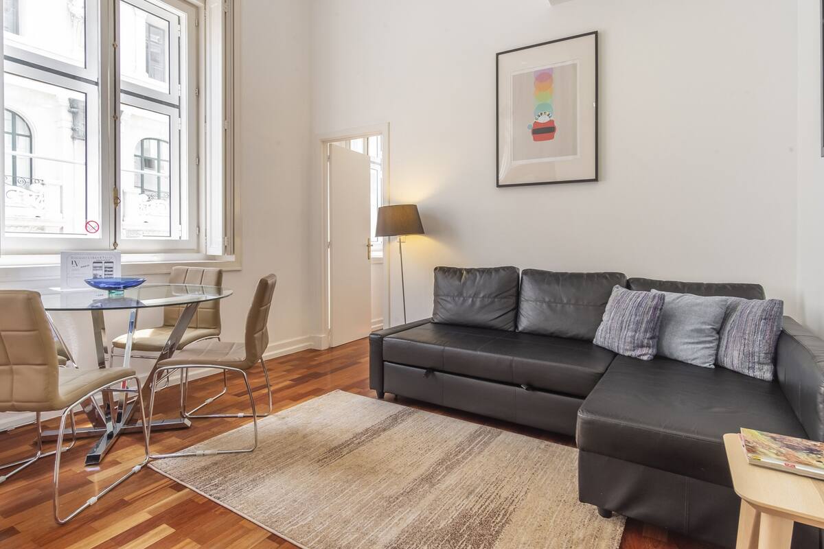 A modern living room with a glass dining table, leather sofa, and a framed picture on the wall.