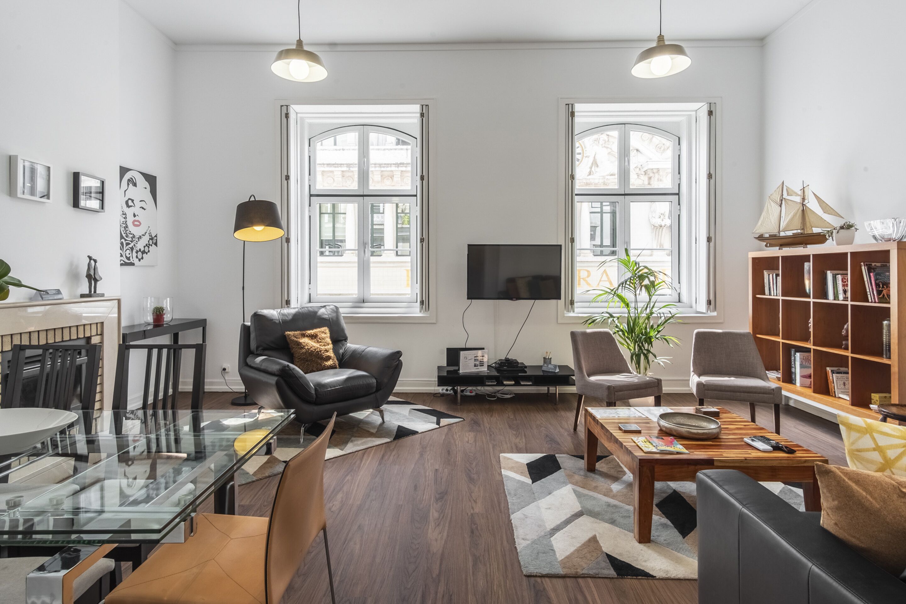 A modern living room with a glass dining table, leather sofas, a wooden coffee table, and a bookshelf.