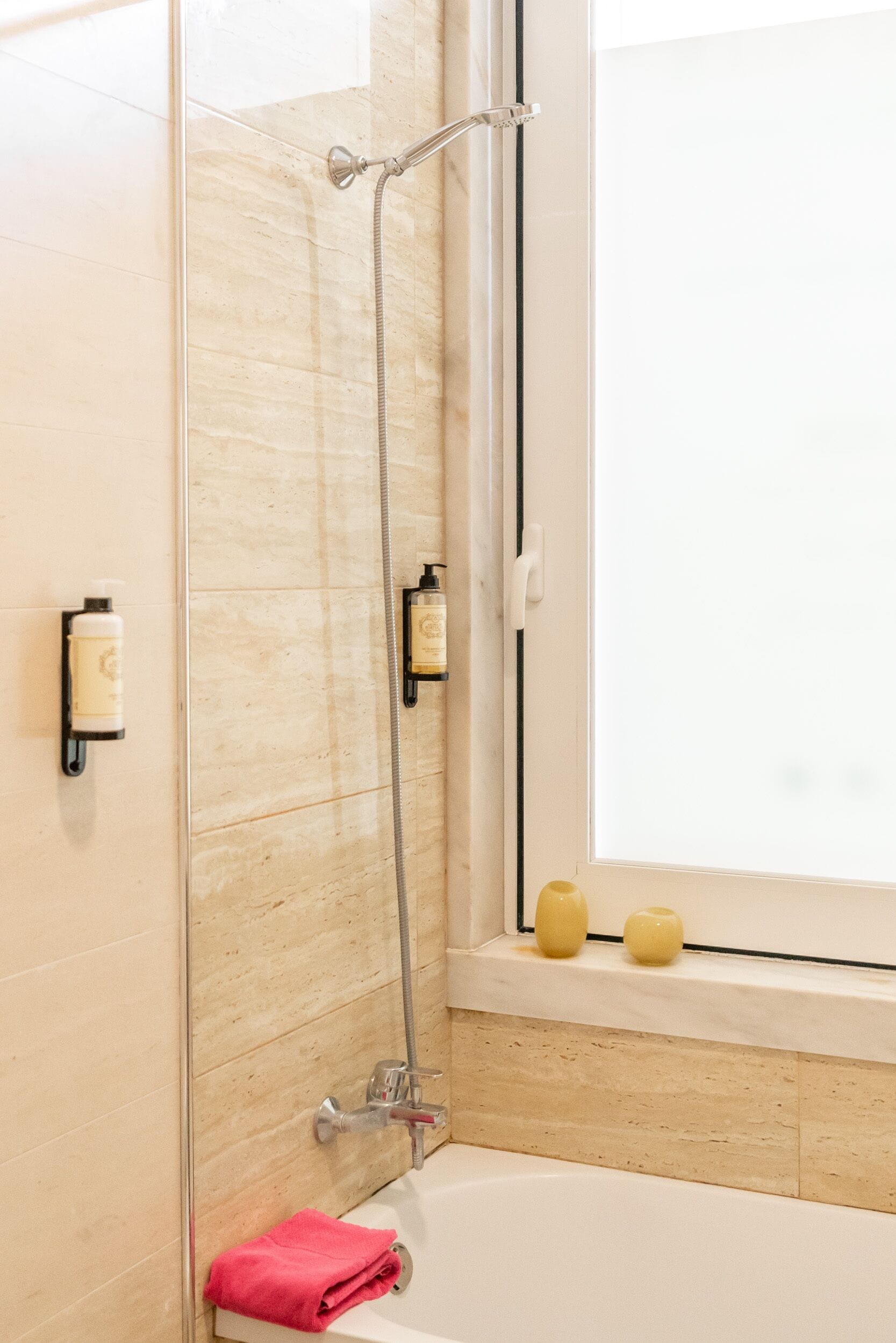 Un baño con ducha envuelta en vidrio, una bañera y dos botellas de artículos de aseo en la pared.