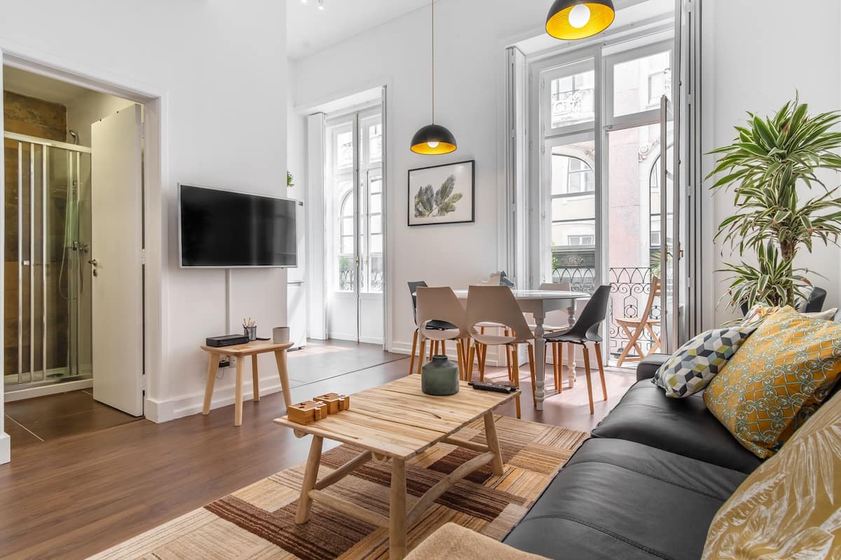 A modern living room with a wooden coffee table, a black sofa, and a TV mounted on the wall.