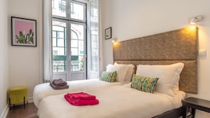 Habitación de hotel con dos camas, un ventanal grande, un taburete amarillo y una lámpara fijada a la pared.