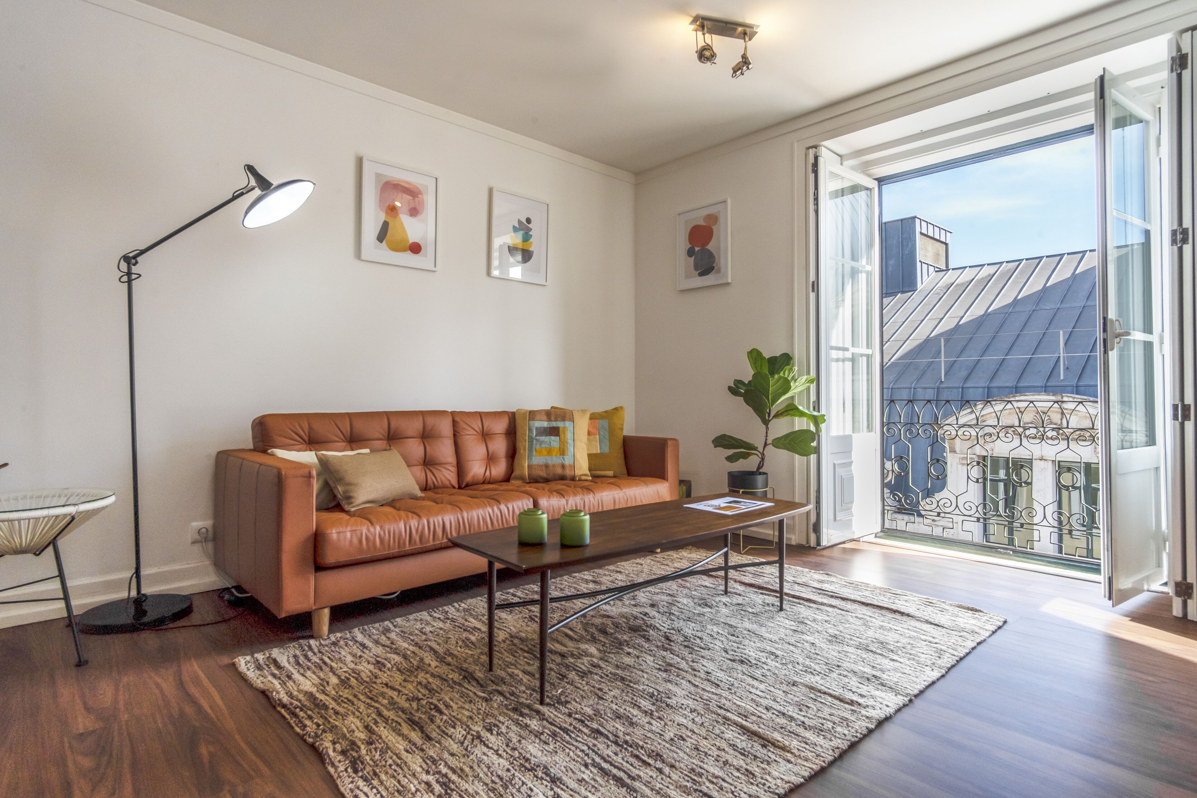 A modern living room with a leather sofa, a coffee table, a floor lamp, and a large window with a view of a building.