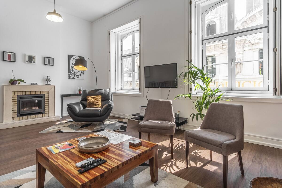 A modern living room with a fireplace, comfortable seating, a flat-screen TV, and large windows offering a view of the city.