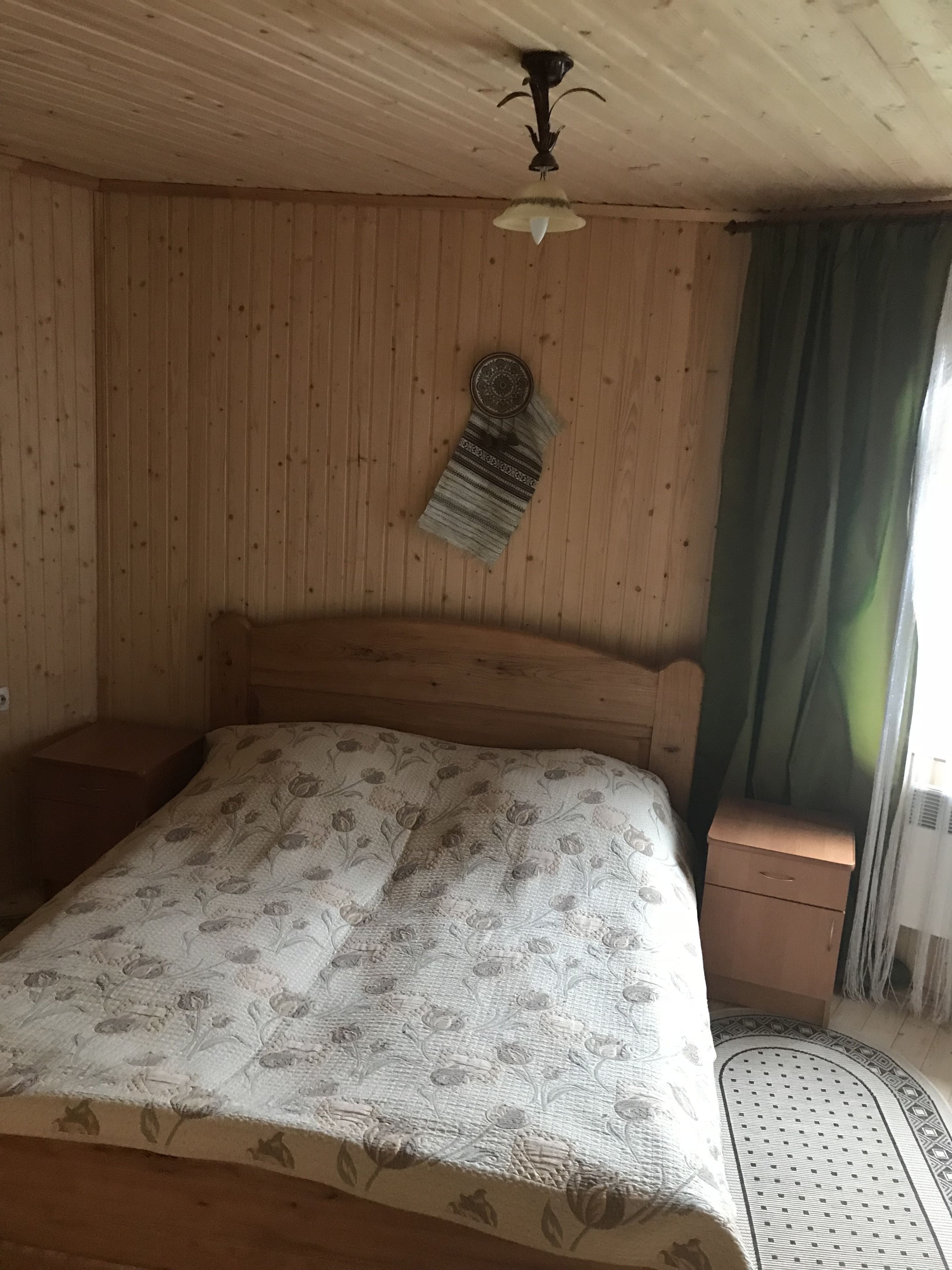 Una habitación con paneles de madera, una cama, una mesita de noche, una lámpara de pared y un ventanal con cortinas.