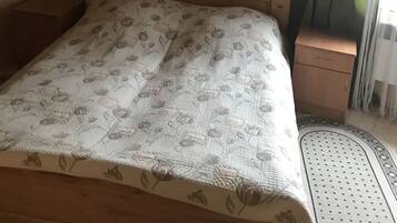 Una habitación con paneles de madera, una cama, una mesita de noche, una lámpara de pared y un ventanal con cortinas.